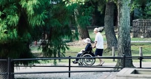 Pflegender Angehöriger schiebt Partnerin mit MS im Rollstuhl durch einen Park