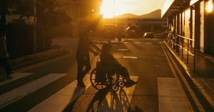 Person hilft anderen Person im Rollstuhl über Strasse